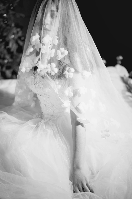 一个黑白照片 新娘穿着婚纱和头纱 走在 aisle 上。