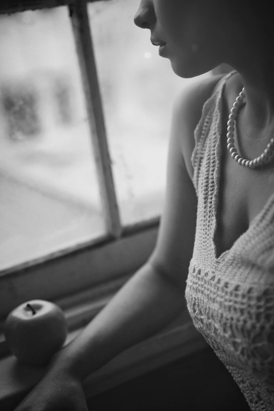 一张黑白照片 一位年轻女士正在窗户边 手里拿着一颗苹果。