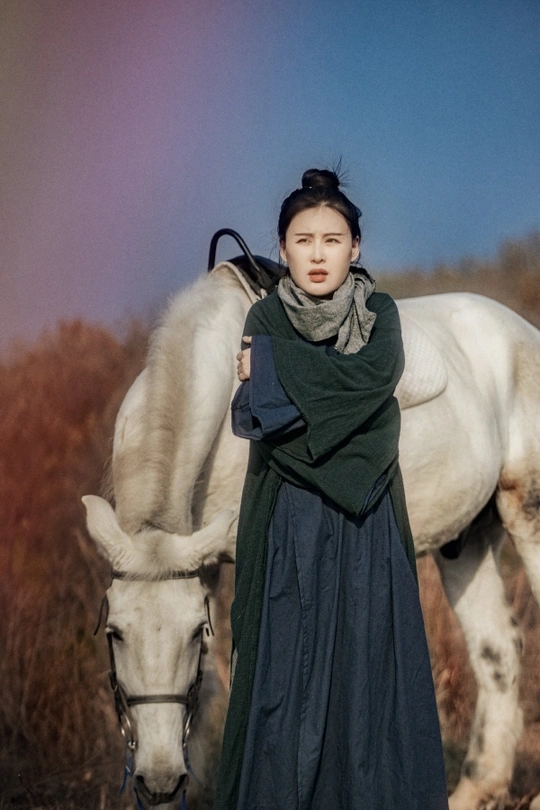 一个穿着连衣裙的年轻女子站在一匹白马旁边