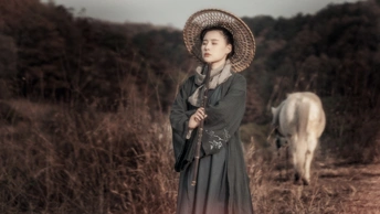 一位穿着连衣裙和帽子站在田野里 旁边有一匹马和一头牛的年轻女子。