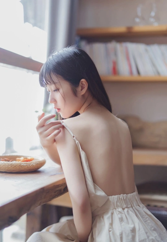 一个穿着连衣裙的年轻女子坐在桌子旁 从杯子中吃食物。