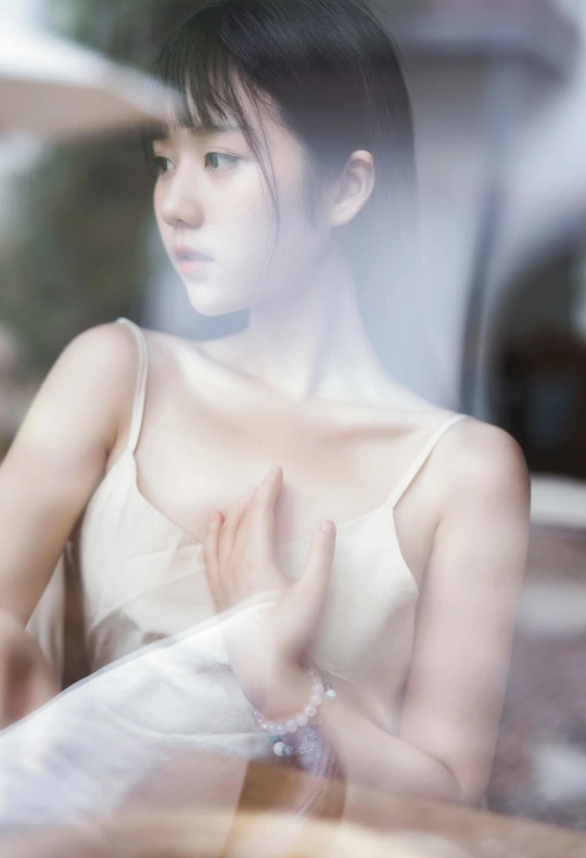 一个穿着白色连衣裙的年轻女子坐在窗后