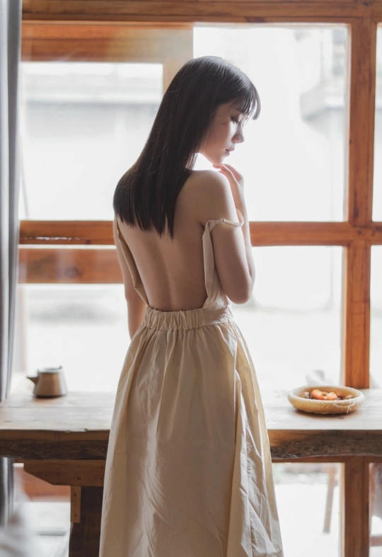 一位穿着白色连衣裙的年轻女子正在窗户旁向外看