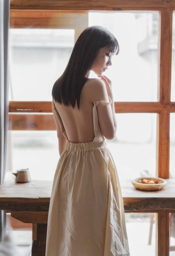 一位穿着白色连衣裙的年轻女子正在窗户旁向外看