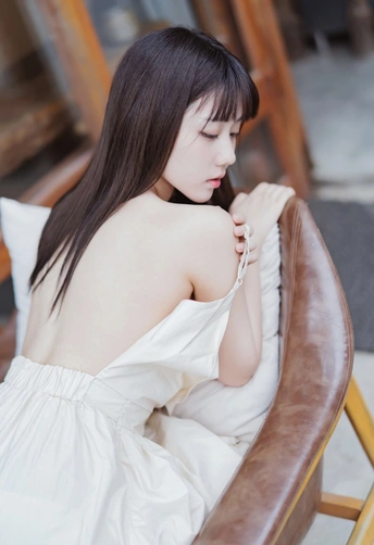 一个穿着白色连衣裙的年轻女子坐在一个棕色椅子上