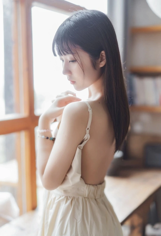 一位穿着白色连衣裙的年轻女子正在窗户旁向外看