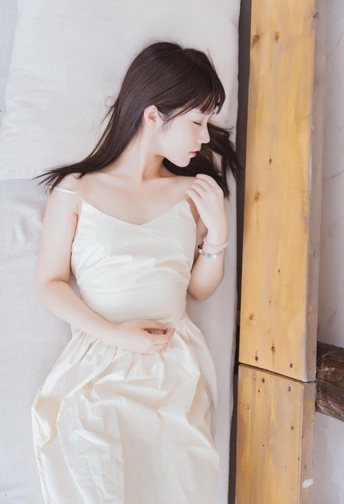 一个美丽的年轻女子穿着白色连衣裙躺在床上