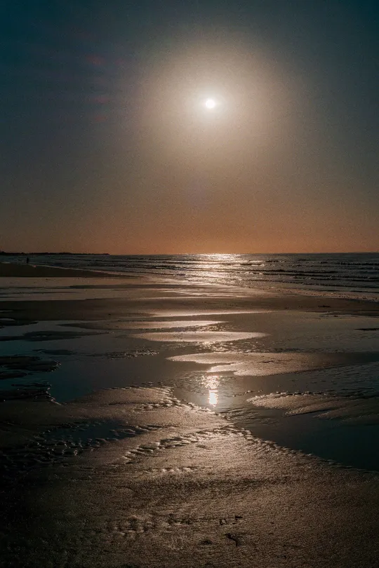 夜晚的海滩 月亮在天空中照耀 满月在水面上反射 湿沙上泛着月光。