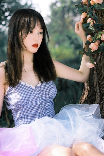 一个穿着蓝白相间连衣裙的年轻女子坐在一棵开着粉色花朵的树下