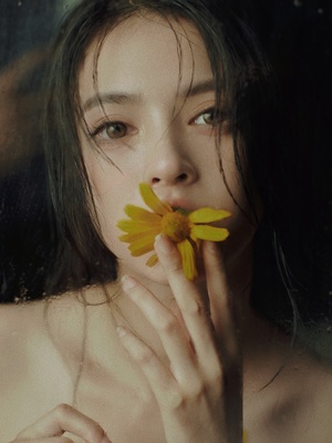 一位年轻女子用手捂着脸闻着一朵黄色的花