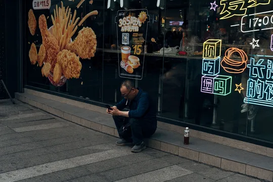 坐在商店前人行道上 窗户里有霓虹灯的男人