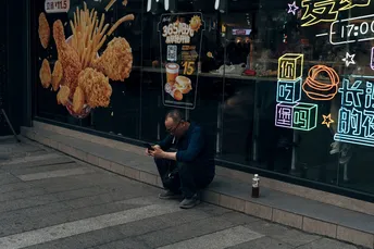 坐在商店前人行道上 窗户里有霓虹灯的男人
