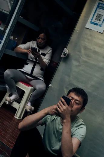 一个人在镜子前用手机自拍 背景有其他人坐着。