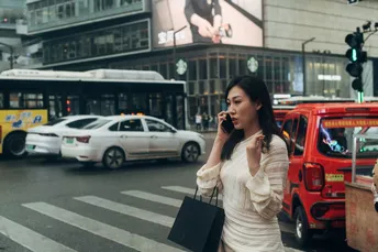 一个穿白色连衣裙的女人在繁忙的街道上走过 同时还在用手机通话。