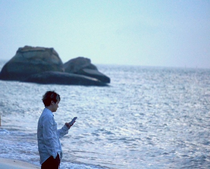 一个人和一个女人在沙滩上行走 注视着海洋和远处的岩石。