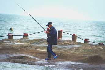 在海洋或海边的岸边钓鱼的男子 手持鱼竿
