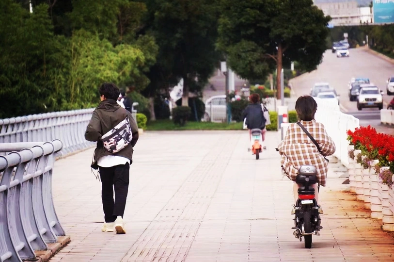 一个男子骑着滑板在人行道上行驶 旁边是街道 人们正在走动和骑自行车。