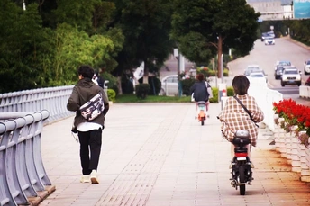 一个男子骑着滑板在人行道上行驶 旁边是街道 人们正在走动和骑自行车。