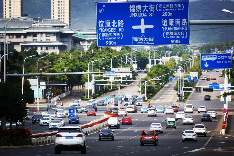 一条充满交通的城市街道 上方有蓝色的路牌。
