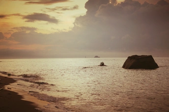 夕阳海滩上 有船在水中 海中有岩石。