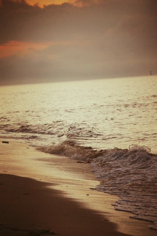 一个带着冲浪板的女人沿着沙滩走 而一个在夕阳下走向海洋的男人走在沙子上。