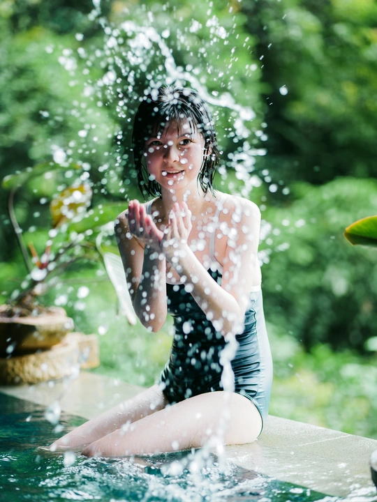 一位年轻女子坐在游泳池边缘戏水溅水