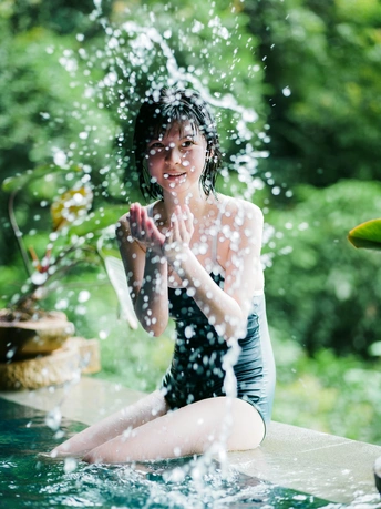 一位年轻女子坐在游泳池边缘戏水溅水