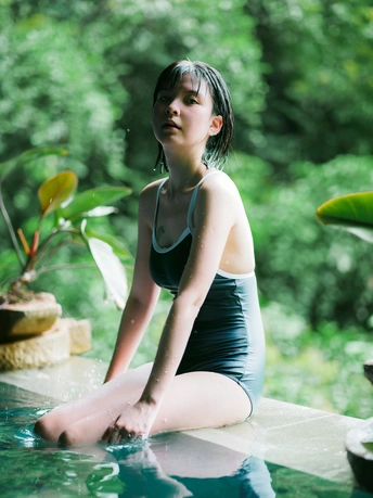 一个年轻女子坐在游泳池边 背景有植物。