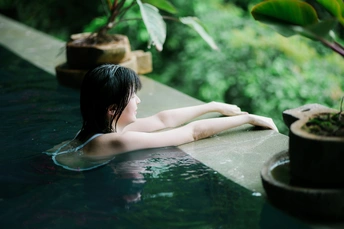 一个年轻女子在有植物背景的热水池中放松。