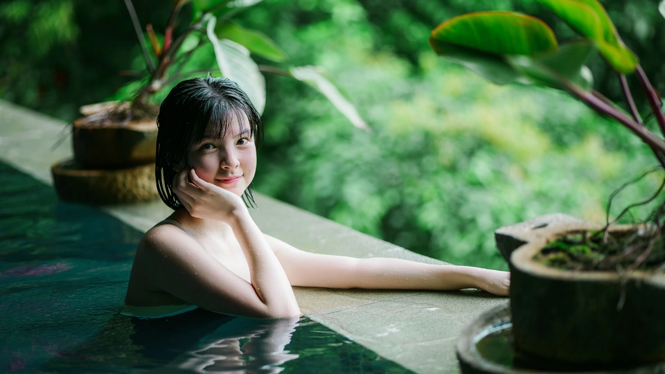 一个年轻女子坐在一个有植物背景的热水浴缸里