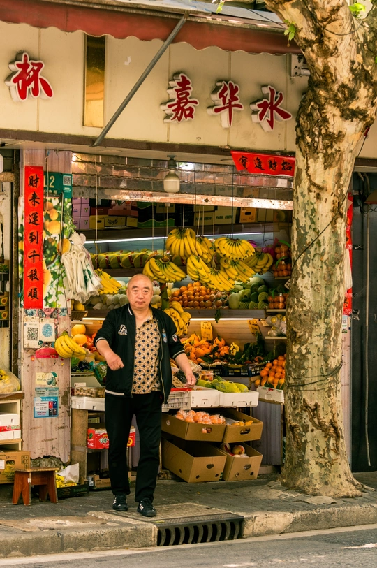 站在一家商店前 商店里有香蕉和其他水果的 sidewalk 上的一个男人