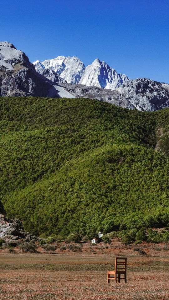 一张木制长凳坐在一片绿草地上 位于一座大型山脉前面。