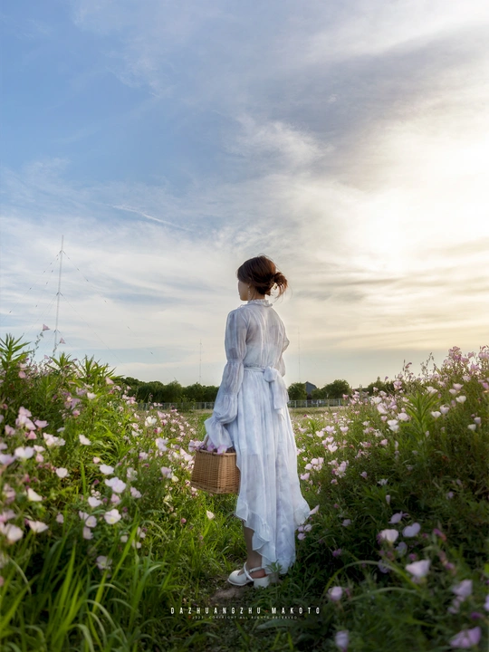 一个穿着白色连衣裙的年轻女子 手拿篮子穿过一片花田。