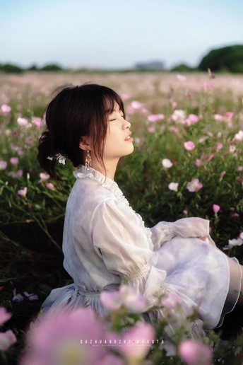 一位穿着白色连衣裙的美丽年轻女子坐在紫花丛中