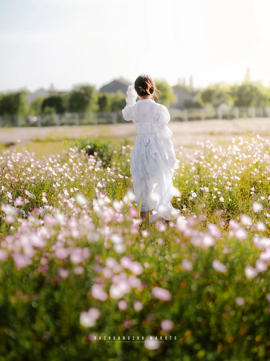 一位穿着白色连衣裙的年轻女子穿过一片花田