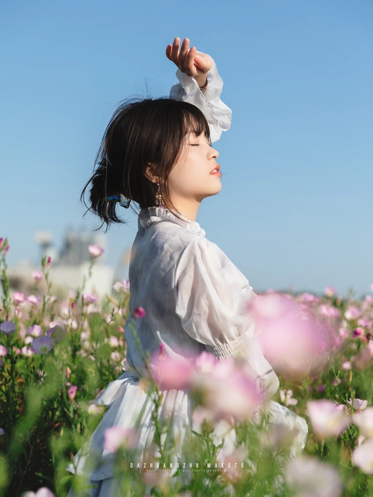 一位穿着白裙子的年轻女子在蓝天下田野中采花