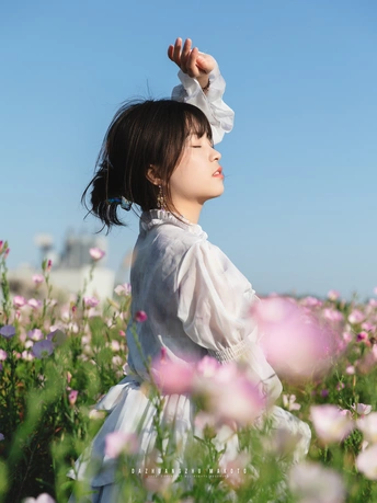 一位穿着白裙子的年轻女子在蓝天下田野中采花