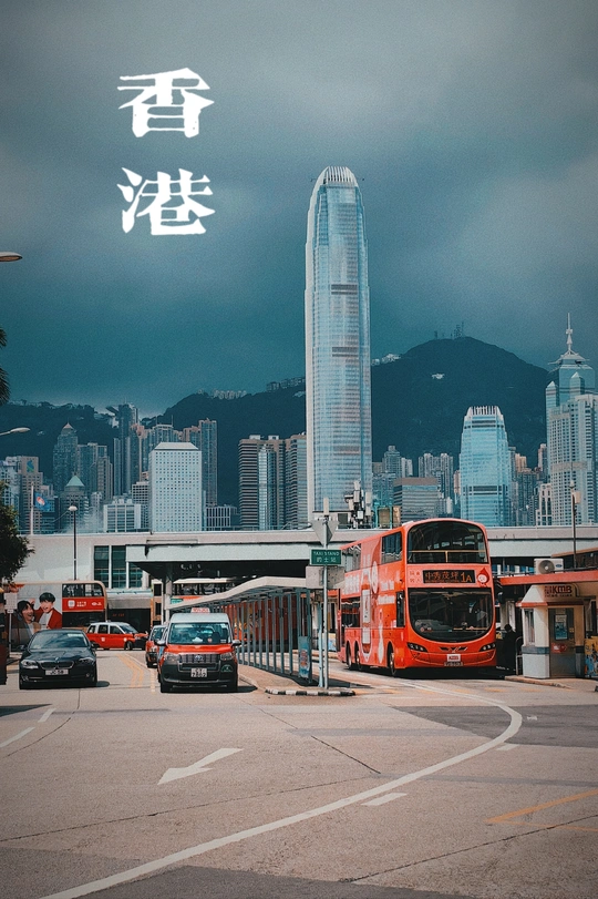 一辆红色的双层公交车在大城市的街道上行驶 街道两旁有高耸的建筑物。