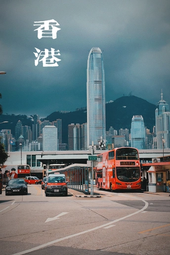 一辆红色的双层公交车在大城市的街道上行驶 街道两旁有高耸的建筑物。