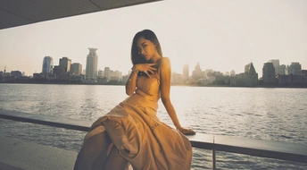 一位穿着连衣裙的女人 倚靠在阳台栏杆上 俯瞰着一片水域和城市。