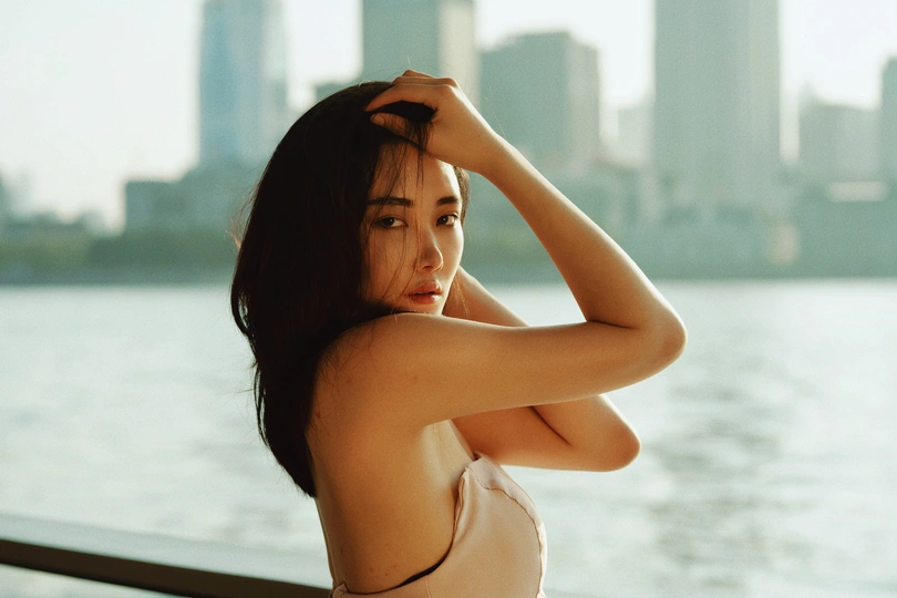 一位穿着比基尼的年轻女子在阳台上俯瞰水面和城市天际线。