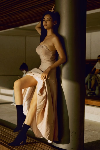 一位穿着连衣裙和高筒靴子的女性坐在靠近杆子的长凳上