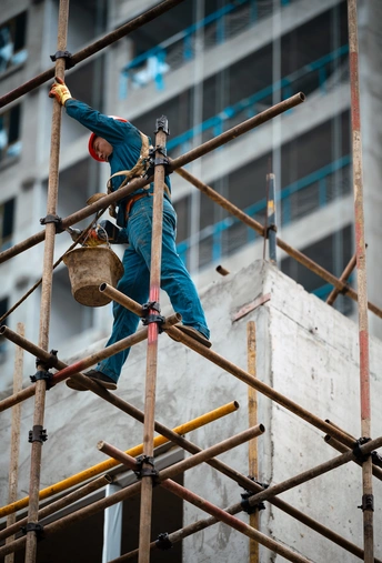 站在脚手架上工作的男人正在一座正在建造的高楼大厦上用桶装混凝土。