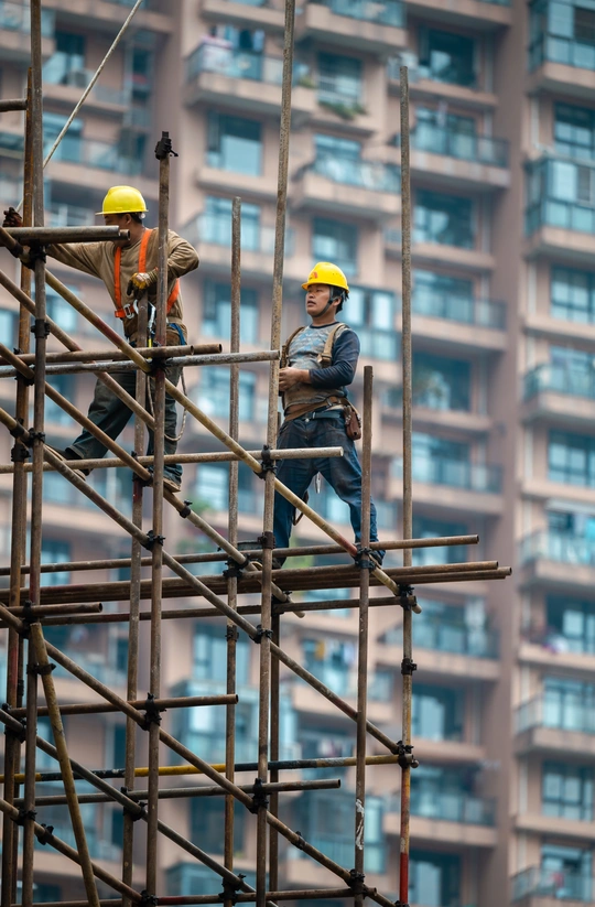 一名建筑工人站在正在施工的高楼脚手架前