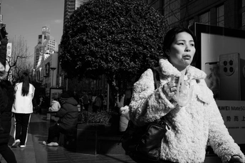 一张黑白照片 一个年轻女孩穿着一件皮草大衣走在繁忙的街道上。