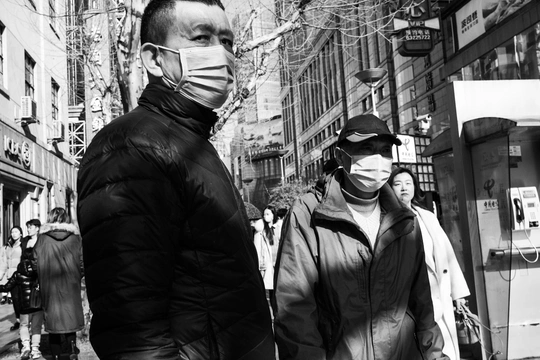 一个戴黑白口罩的男子走在街上 一名女子站在人行道上。