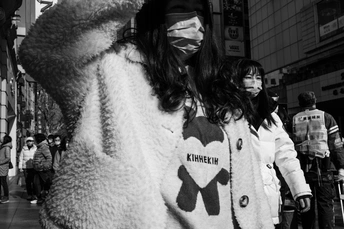 一位戴着手套和面罩的女士走在街上 周围有其他人。