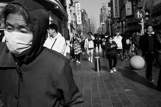 一个戴面具的男子站在一把雨伞下 人们走过一条繁忙的街道。