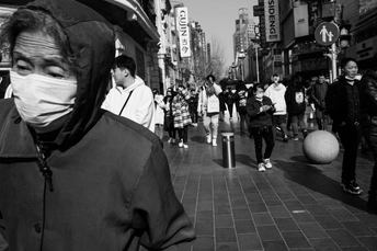 一个戴面具的男子站在一把雨伞下 人们走过一条繁忙的街道。