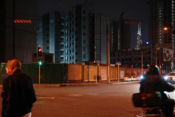 夜晚的城市街道 一名男子骑摩托车 前景中有人步行 背景中有建筑物。